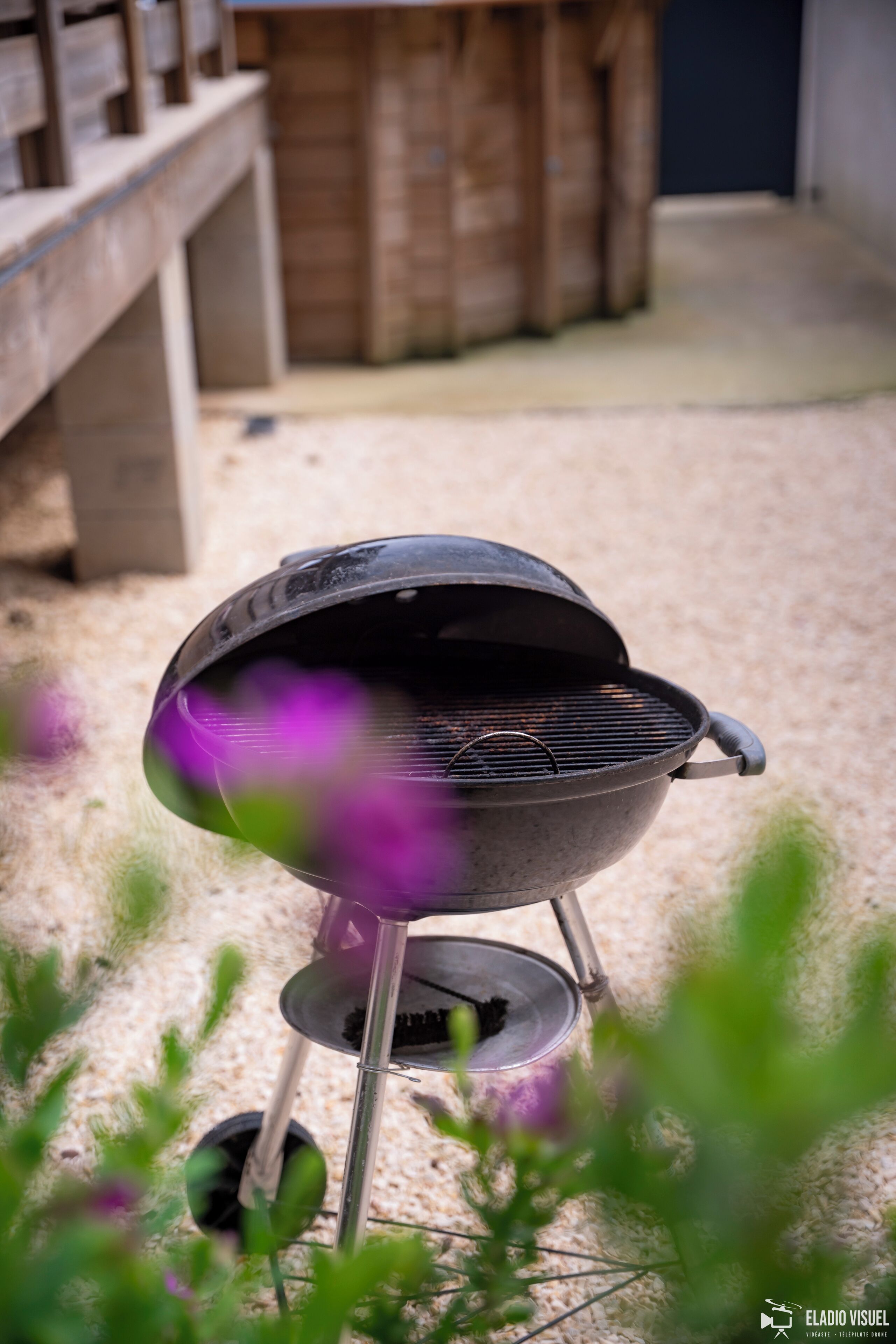 A portable grill in a backyard with a wooden fence and a concrete structure in the background.