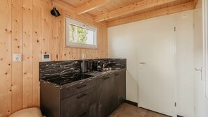 Una cocina compacta con paredes de madera, encimera de mármol y una puerta blanca.