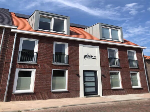 A red brick building with multiple windows and balconies, a prominent entrance with a sign, and a flat roof with skylights. - Lodge With a Magnificent View of the Dunes (Zoutelande)