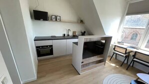 A modern kitchen with a built-in oven, a small island with a sink, and a window overlooking a brick building. - Lodge With a Magnificent View of the Dunes (Zoutelande)