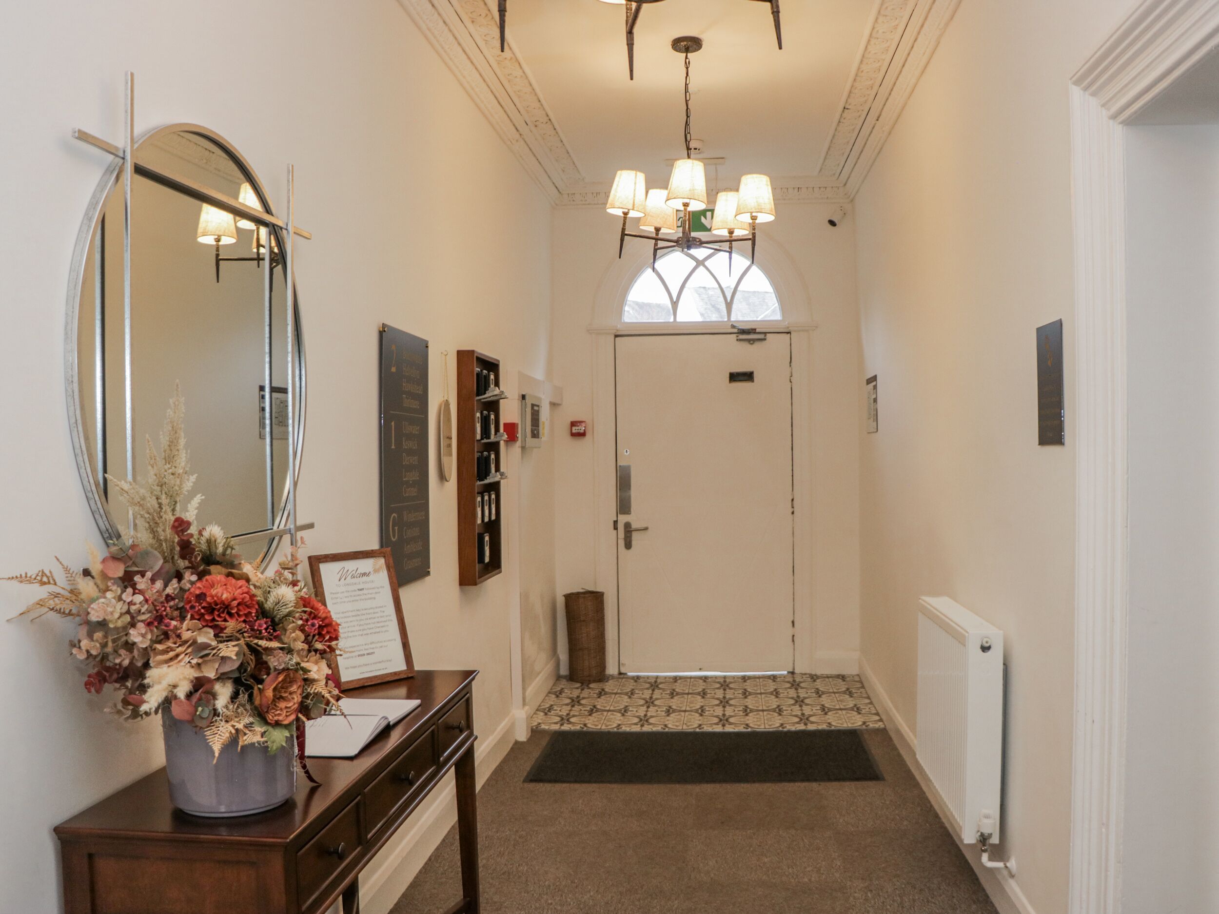 A reception area with a desk, a large mirror, a chandelier, a door, and a bulletin board.