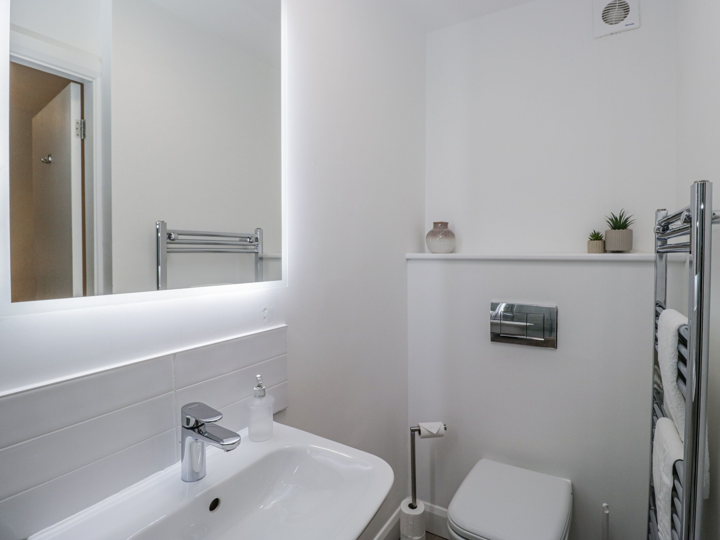 Un baño moderno con un lavamanos blanco, un inodoro, un perchero para toallas y un espejo.
