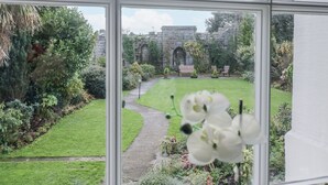 A view through a window of a garden with a stone wall, a pathway, and a bench. - Derwent (Ulverston)