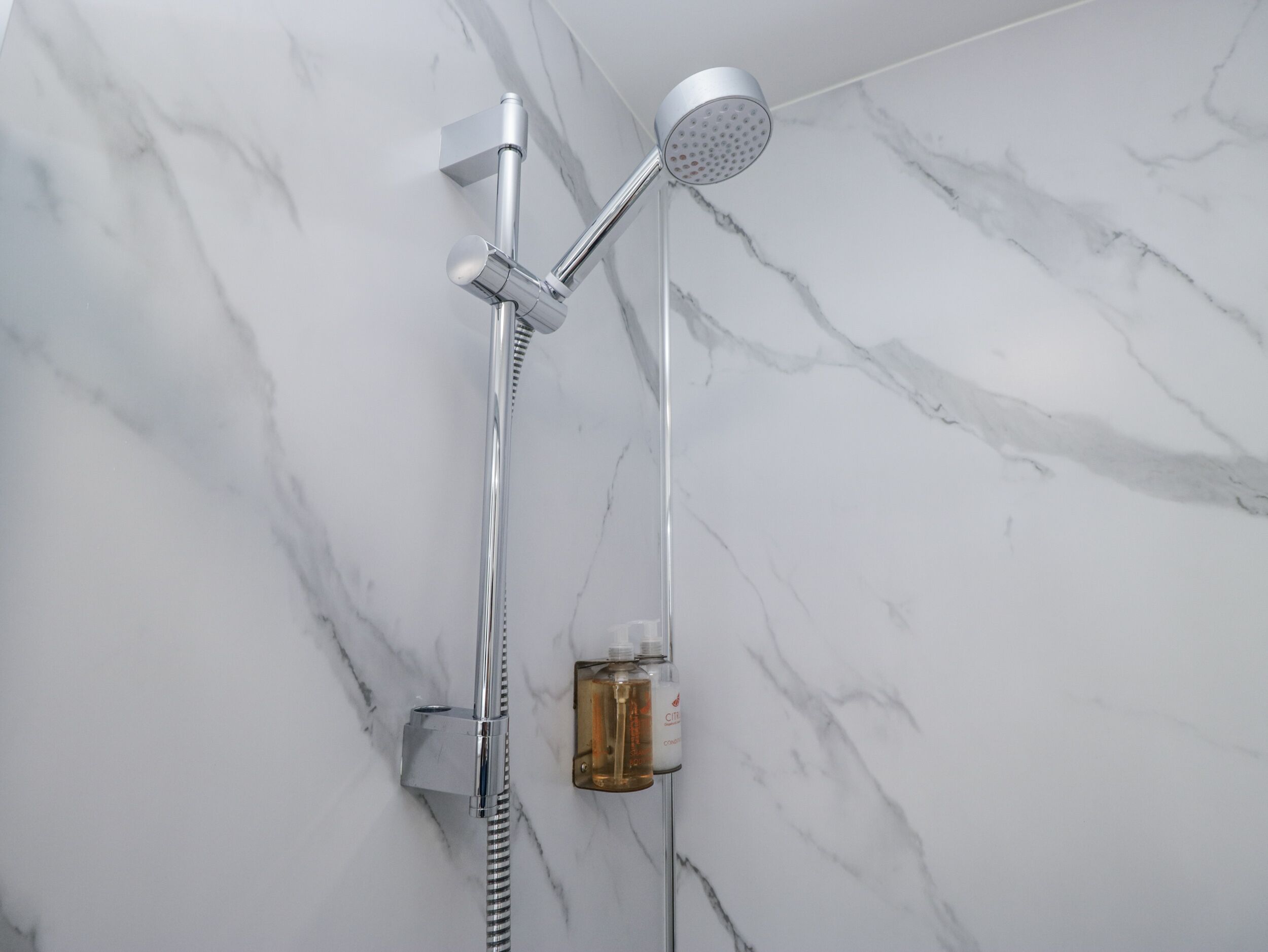 A modern shower with a handheld showerhead and a fixed showerhead, mounted on a wall with a marble pattern.