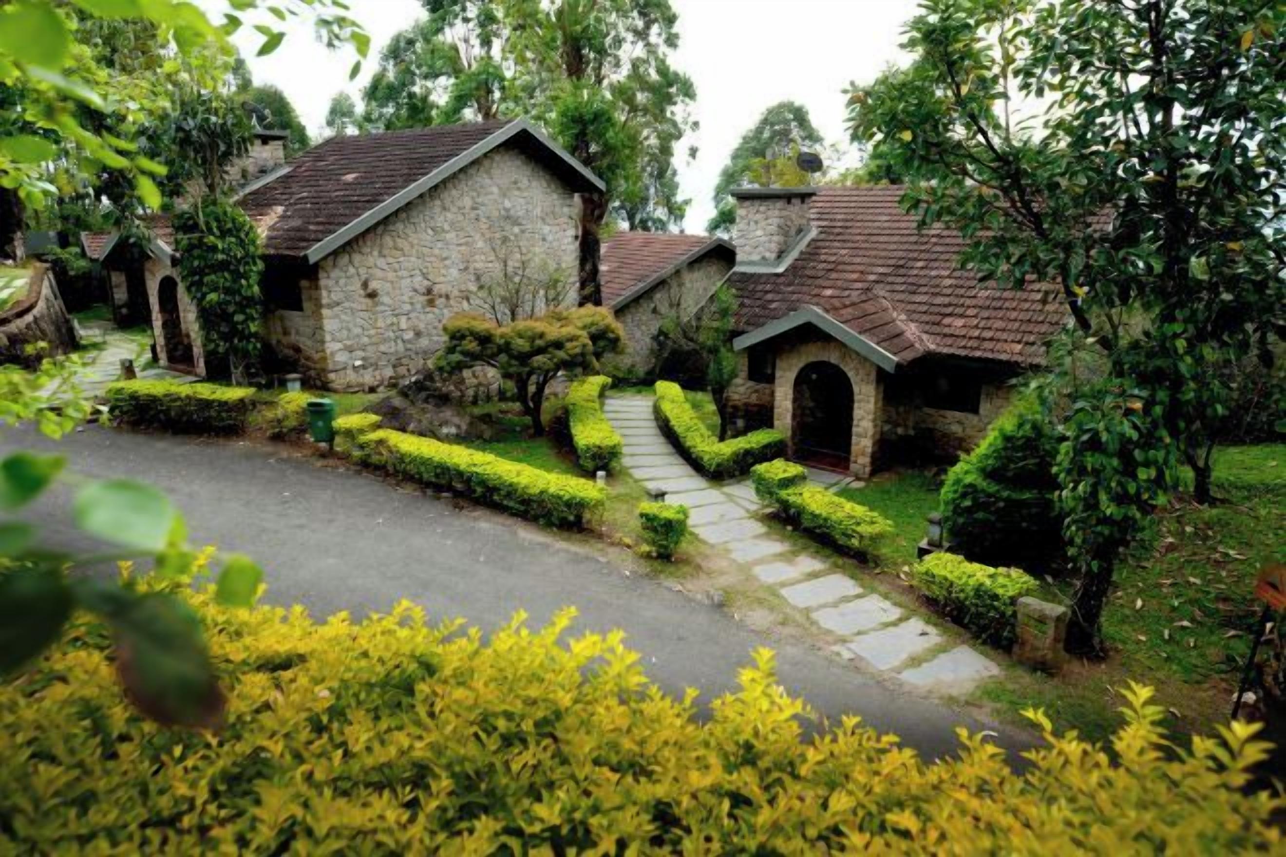 A stone building with a tiled roof, surrounded by well-maintained hedges and a paved driveway.