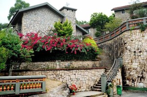 Un edificio de piedra con una escalera que lo conduce, rodeado de follaje y flores.