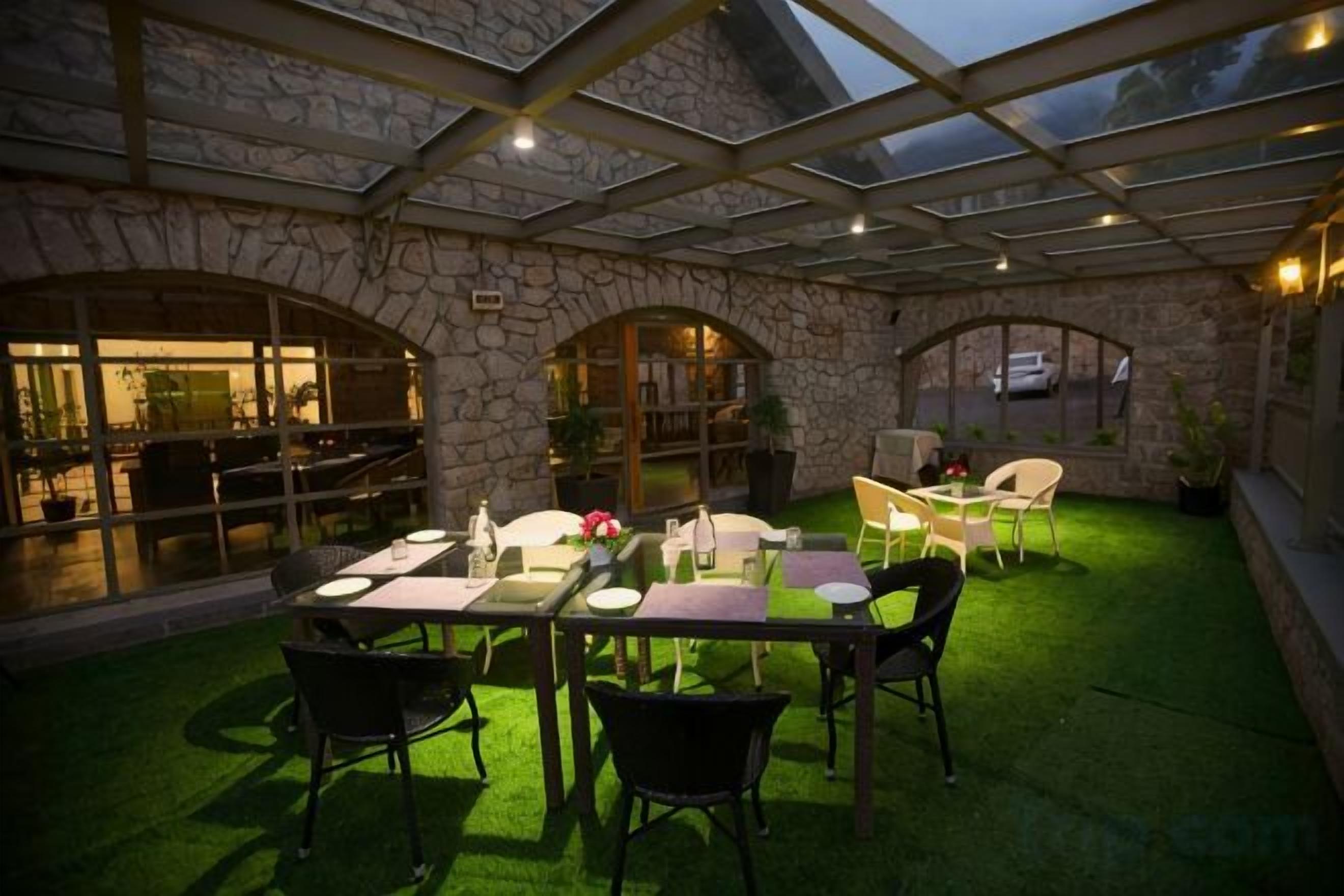 Un patio al aire libre con un muro de piedra, techo de vidrio y área con césped artificial verde.