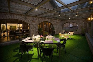 An outdoor patio with a stone wall, a glass roof, and a green artificial turf area. - Mountain Club Resort (Chinnakanal)