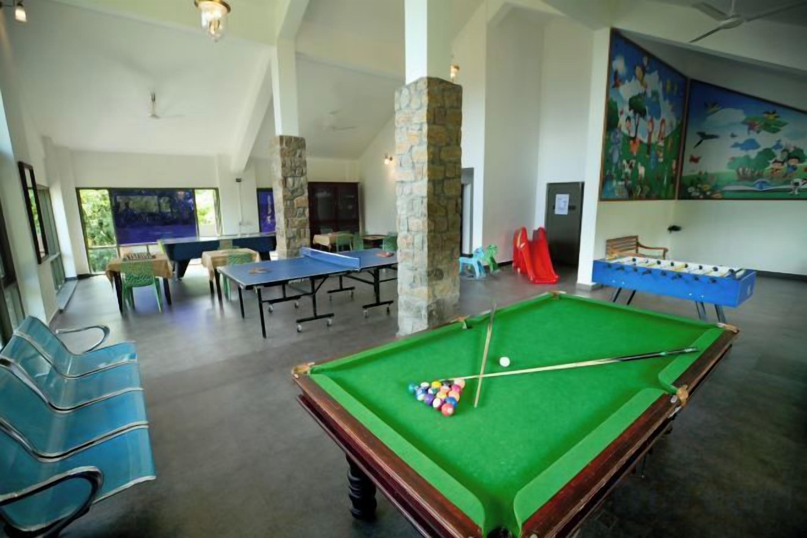 A pool table with billiard balls, a ping pong table, and a foosball table in a spacious room with high ceilings and stone pillars.
