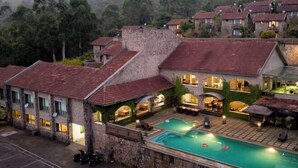 A hotel with a pool, outdoor seating, and a view of the surrounding forest. - Mountain Club Resort (Chinnakanal)