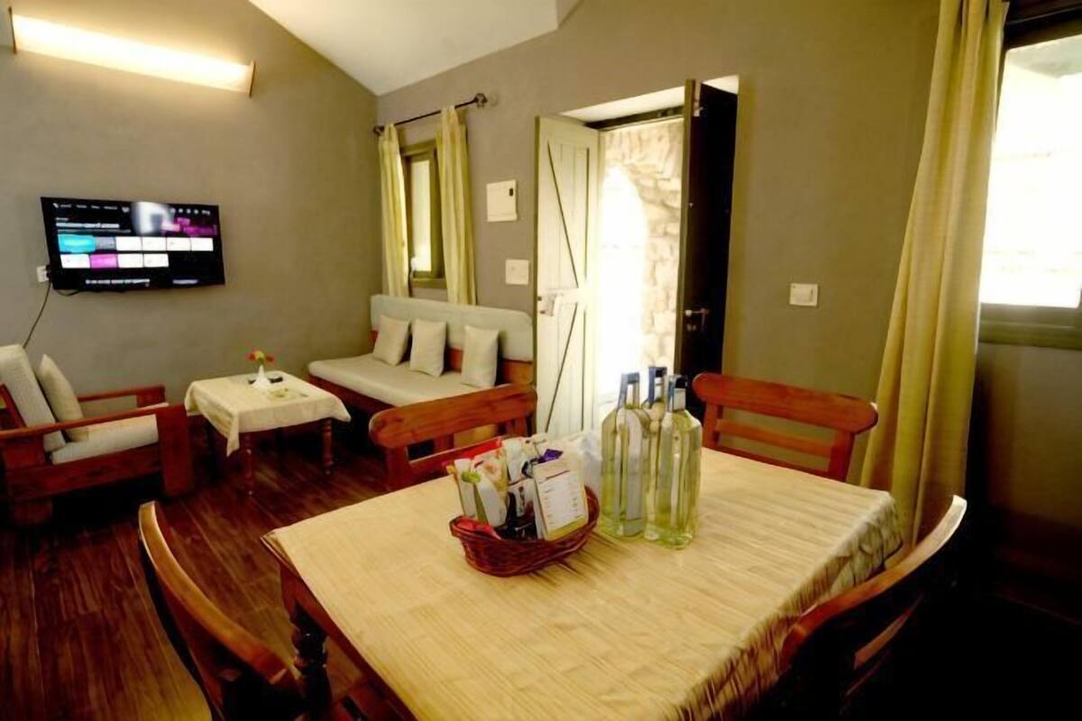 Una habitación de hotel con sofá, una mesa pequeña, televisor y una mesa de comedor con botellas.