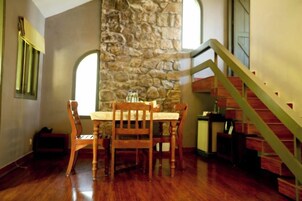 Un comedor con pared de piedra, mesa y sillas de madera.
