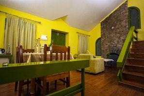A room with a dining table, a sofa, a staircase, and a stone wall. - Mountain Club Resort (Chinnakanal)