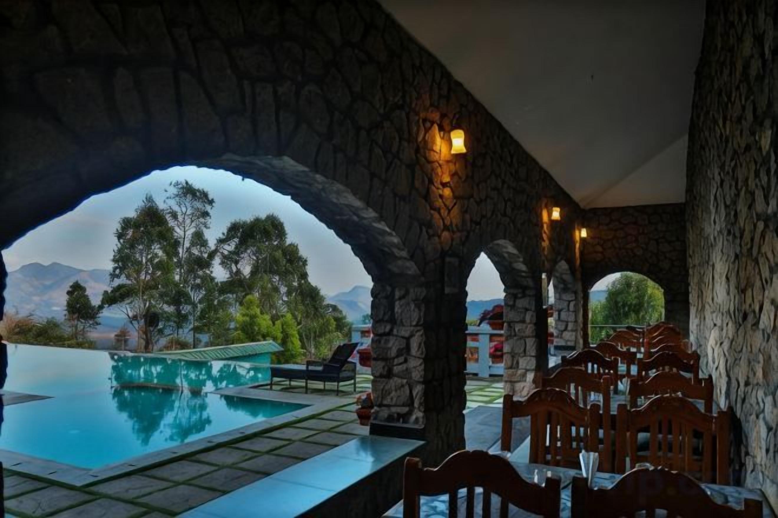 Un arco de piedra que da acceso a una piscina con vistas a árboles y montañas.