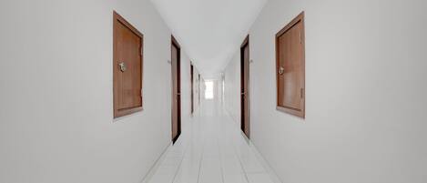Un long couloir étroit, avec un sol carrelé de carreaux blancs et des portes en bois de chaque côté.