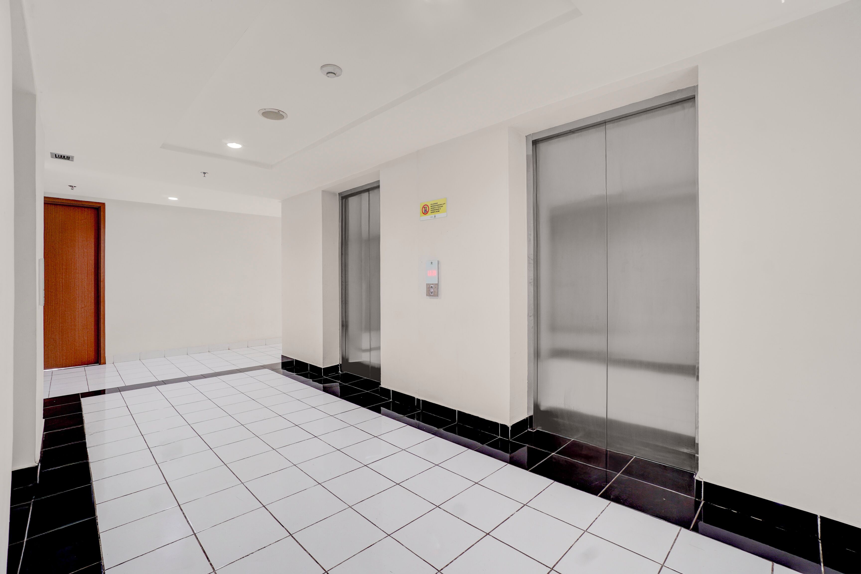 A hallway with white tiled floors, a wooden door, and two elevators.