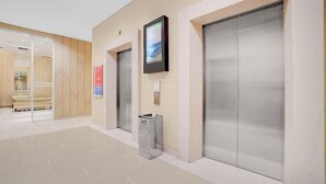 Een modern liftgedeelte met een digitaal scherm, een prullenbak en een zithoek op de achtergrond.