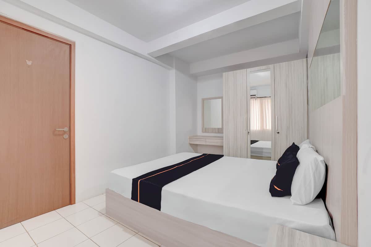 A modern bedroom with a wooden door, a bed with a black and orange bedspread, a bedside mirror, and a large mirror above the bed.