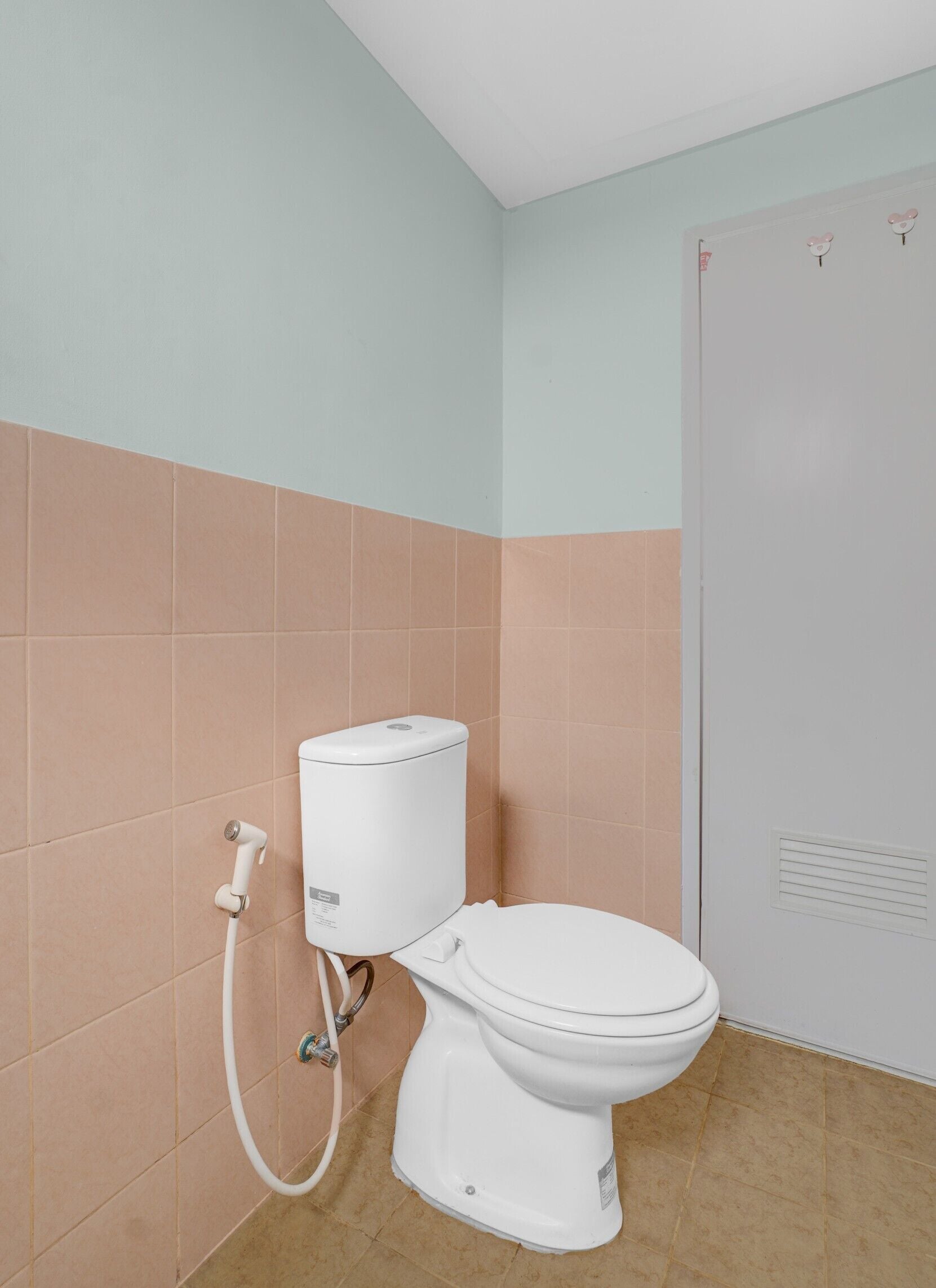 A bathroom with a toilet, a shower attachment, and a door with a vent.