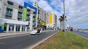 A street with a white car driving past a hotel named 'HOTEL PLAYAMAR' and a yellow building. - Hotel Playamar (Mazatlán)