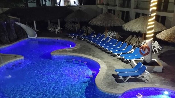 A pool area with blue lighting, lounge chairs, and thatched umbrellas. - Hotel Playamar (Mazatlán)