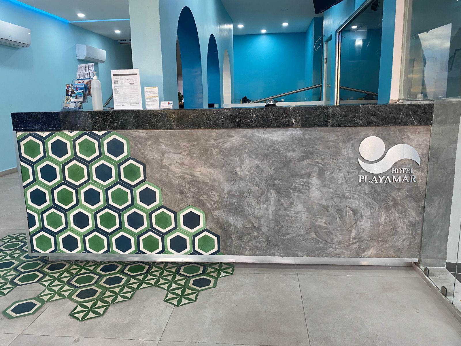 Un mostrador de recepción de hotel con un diseño de baldosas geométricas, un logotipo y una mampara de vidrio.