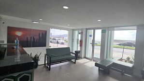 A reception area with a bench, a painting, a reception desk, and a view of parked cars outside. - Hotel Playamar (Mazatlán)