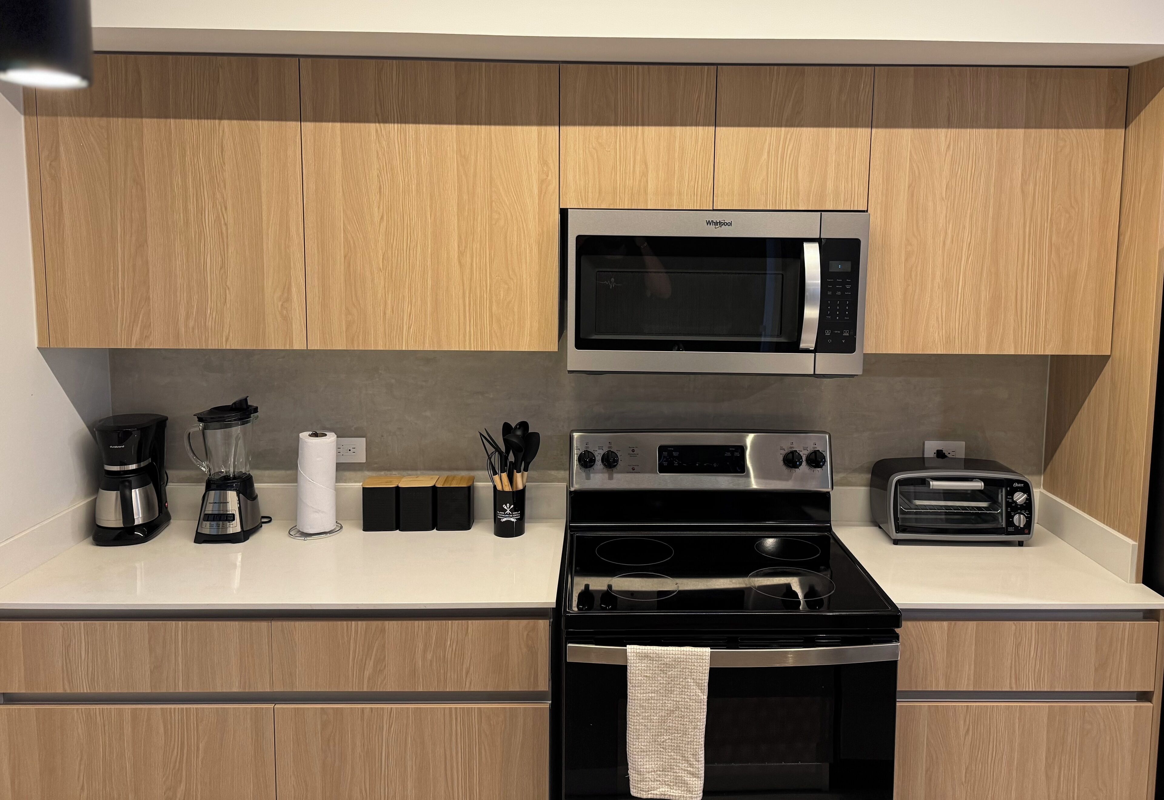 Una cucina moderna con mobili in legno, forno a microonde integrato, piano cottura, tostapane e macchina per il caffè.