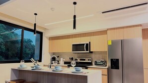 A modern kitchen with a central island, bar stools, a microwave, a stove, a toaster, and a refrigerator. - Bosques de Jacó Condo (Jacó)