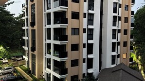 A modern multi-story building with balconies, a swimming pool, and a landscaped garden. - Bosques de Jacó Condo (Jacó)
