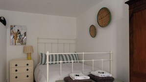 Une chambre à coucher avec un lit en métal blanc, une table de chevet avec une lampe et deux paniers fixés au mur.