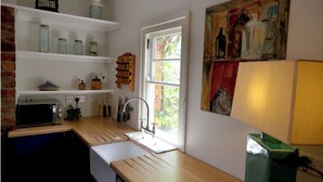 Une cuisine compacte équipée d’un four à micro-ondes, d’un évier et d’un plan de travail en bois. On y trouve des étagères remplies de bocaux et un tableau accroché au mur.