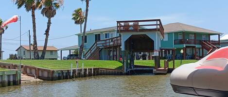 A waterfront property with a covered dock, a two-story building with a balcony, and a grassy area.