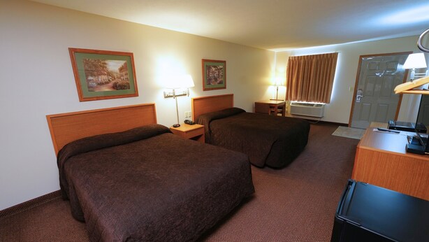 A hotel room with two beds, a desk, a chair, a lamp, and a window with curtains. - Hill Street Inn (Osmond)