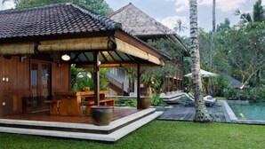 A wooden villa with a thatched roof, a pool, and lush greenery. - Villa Inka Ubud by Nakula (Bali)