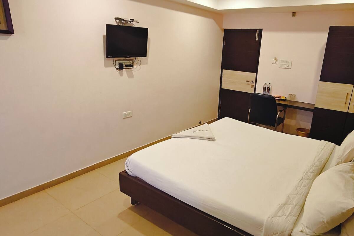 Ein Schlafzimmer mit einem Bett, einem an der Wand montierten Fernseher, einem Kleiderschrank und einem kleinen Tisch mit Gegenständen darauf.