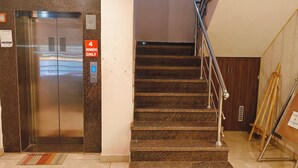 Ein Aufzug mit Hinweisschild für Mitglieder, eine Treppe mit Handlauf und ein Schild an der Wand, das den 1. Stock angibt.