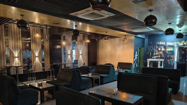 Ein moderner Loungebereich mit dunkel gehaltenen Sitzmöbeln, einer Bar im Hintergrund und dekorativer Beleuchtung.