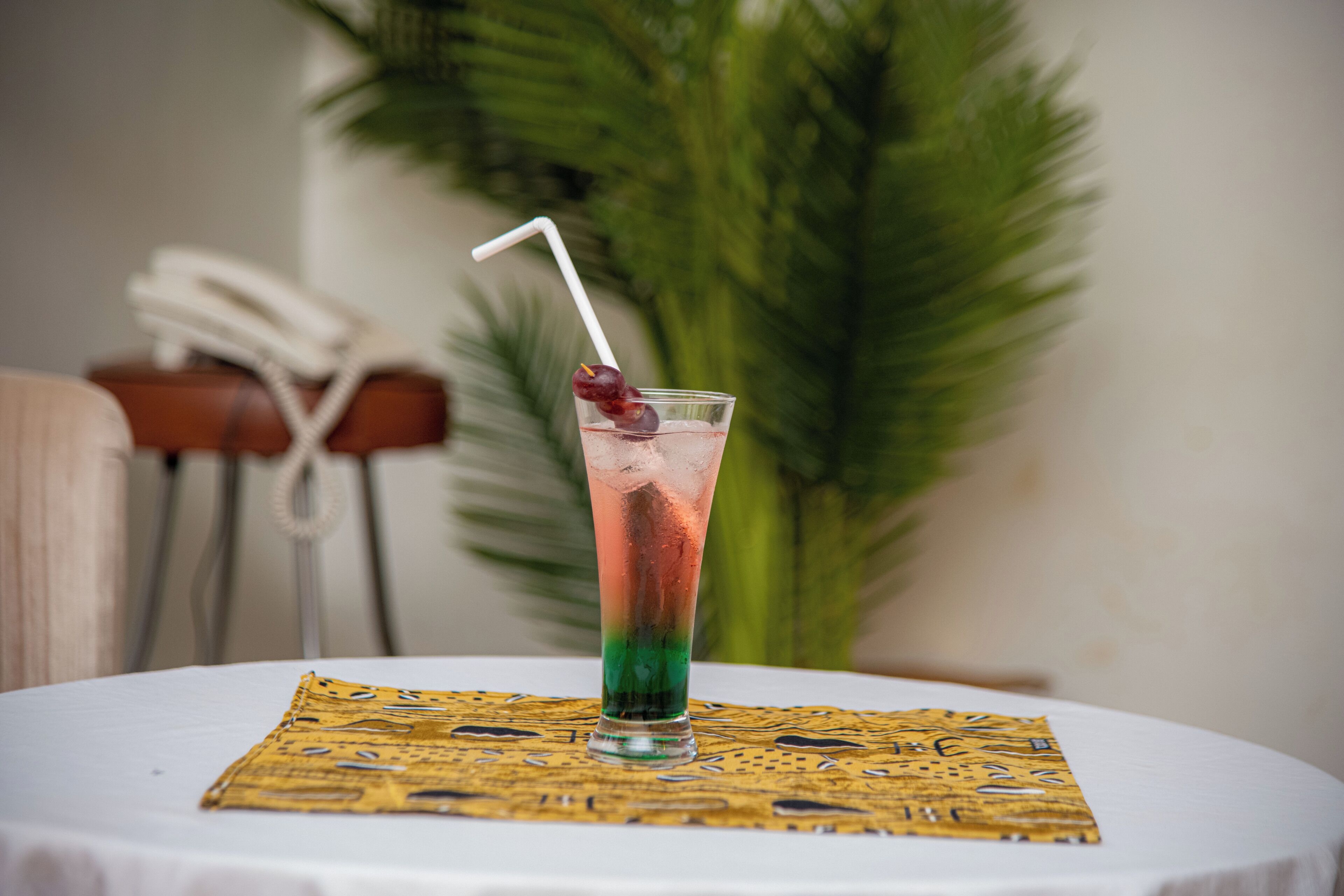 Un cocktail servi avec une paille et une cerise, posé sur une table recouverte d’un set de table à motifs.