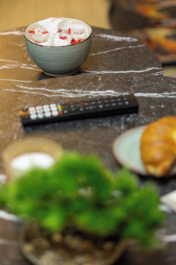 A bowl of snacks, a remote control, a plate with a pastry, and a potted plant on a marble surface. - Grand Chalet Ramina Poiana Brasov (Brașov)