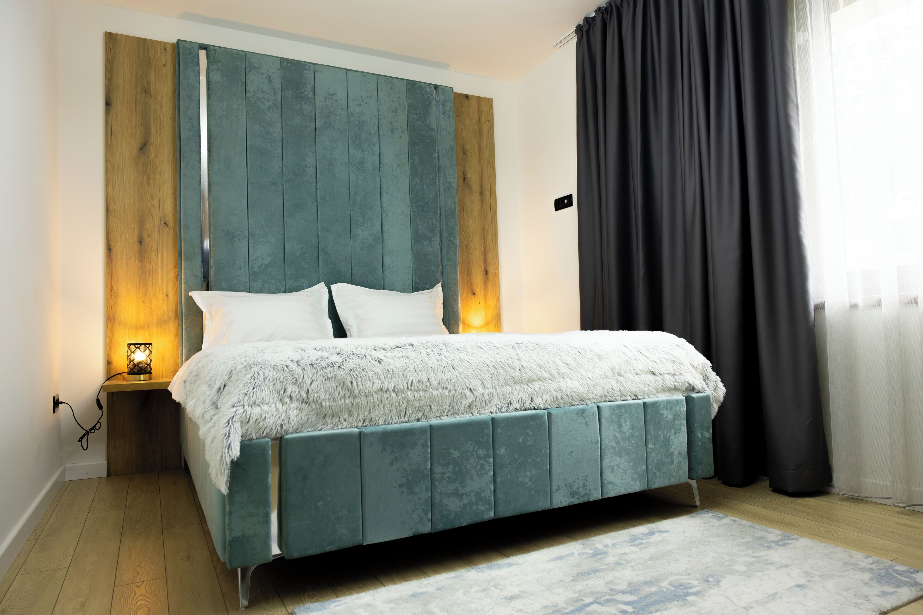 Een moderne slaapkamer met een smaragdgroen bekleden bed, een houten hoofdbord en een nachtkastje met een lamp.