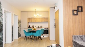 A modern kitchen with wooden cabinets, a dining area with teal chairs, and a marble countertop with a fruit bowl and glass. - Grand Chalet Ramina Poiana Brasov (Brașov)