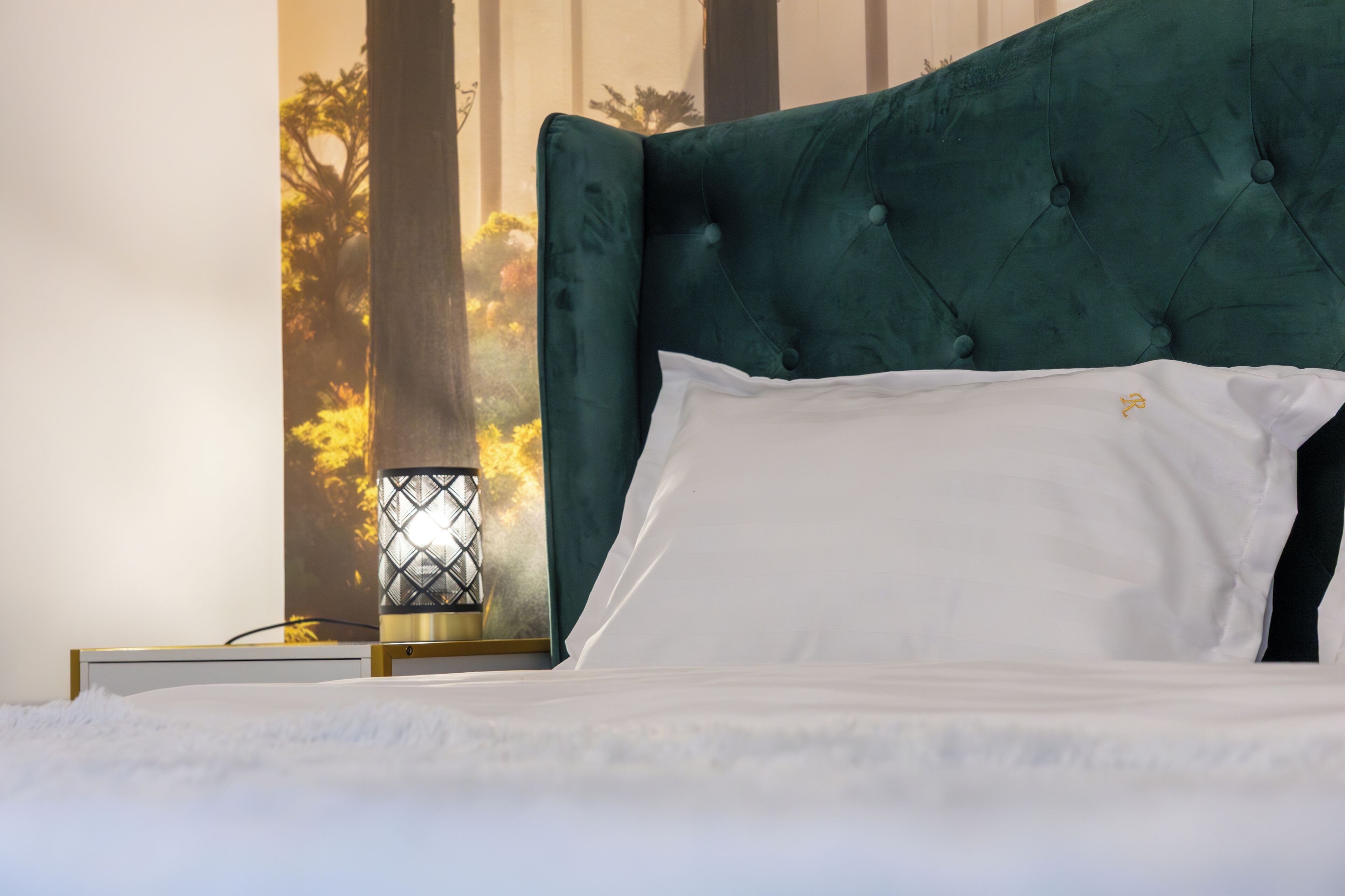 Ein Bett mit einem geblatteten Kopfteil, weißer Bettwäsche und einem kleinen Tisch mit Lampe daneben.