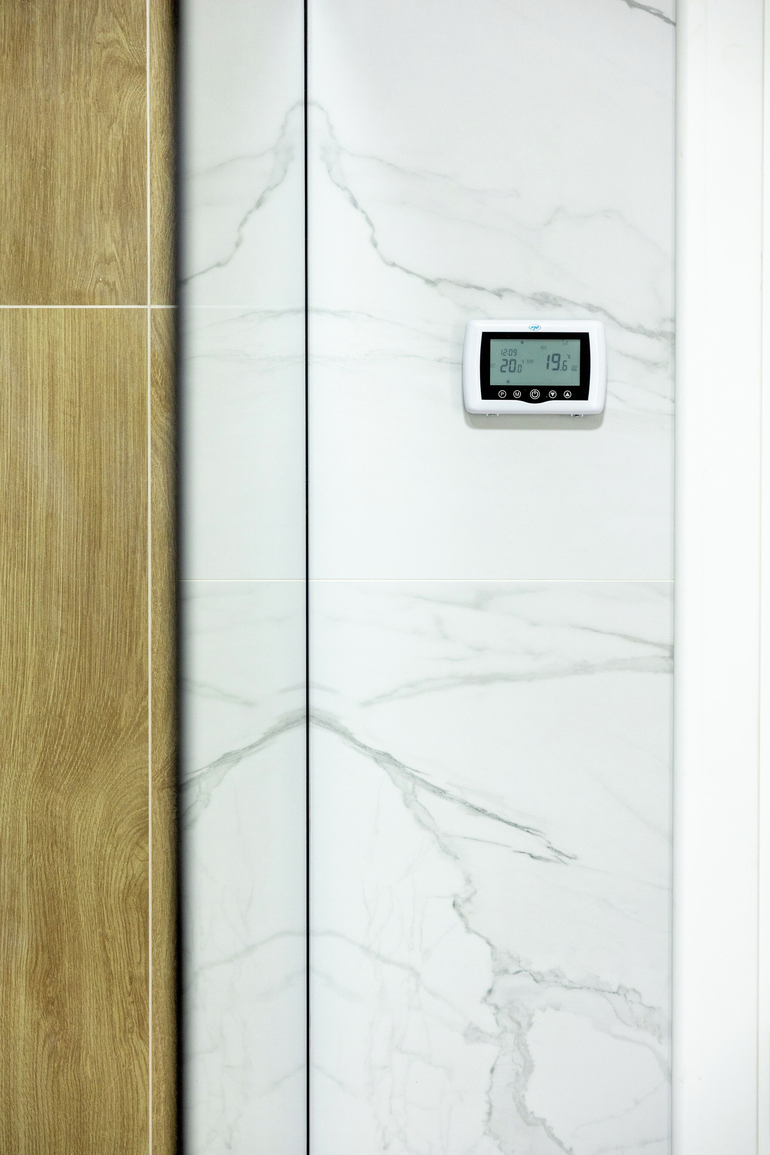 A bathroom with a wooden vanity and a marble wall with a digital thermostat.