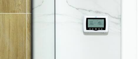 A bathroom with a wooden vanity and a marble wall with a digital thermostat.