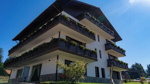 A multi-story building with balconies adorned with plants, a stone base, and a clear blue sky. - Grand Chalet Ramina Poiana Brasov (Brașov)