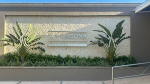 A sign for "LA ASONA Steakhouse & Seafood Grill" with a hexagonal stone wall and two large plants. - Deluxe Ocean View Suite – The Ultimate Luxury Experience in Cancún (Cancún)