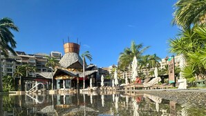 A resort pool area with a thatched-roof structure, palm trees, and a clear blue sky. - Deluxe Ocean View Suite – The Ultimate Luxury Experience in Cancún (Cancún)