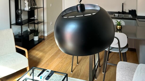 Een moderne woonkamer met een zwarte bolvormige lamp, een glazen salontafel en een grijze bank.