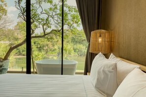 Une chambre avec une grande fenêtre, une baignoire et un lit recouvert de draps blancs.